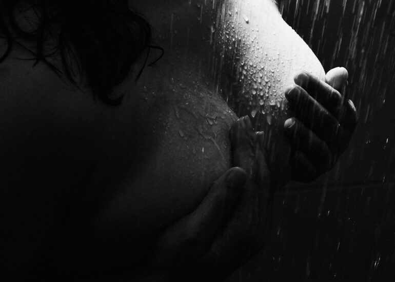 Mulher escondendo os seios com as mãos, debaixo do chuveiro em ensaio boudoir