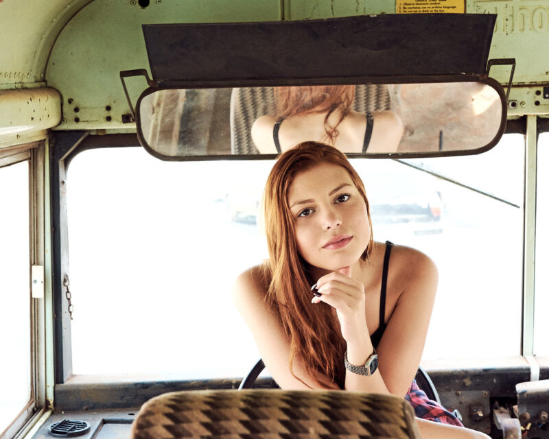 Mulher posando para a câmera debruçada sobre o banco de um ônibus antigo