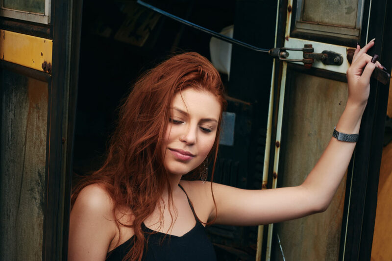 Mulher ruiva posando apoiada na porta de um ônibus antigo