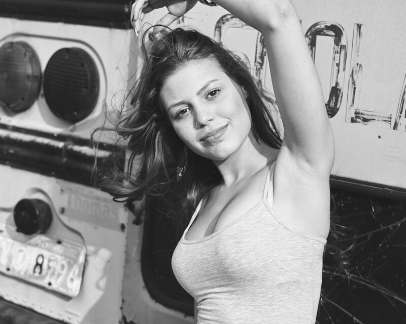 Retrato preto e branco de mulher ruiva passando a mão nos cabelos encostada em um ônibus antigo