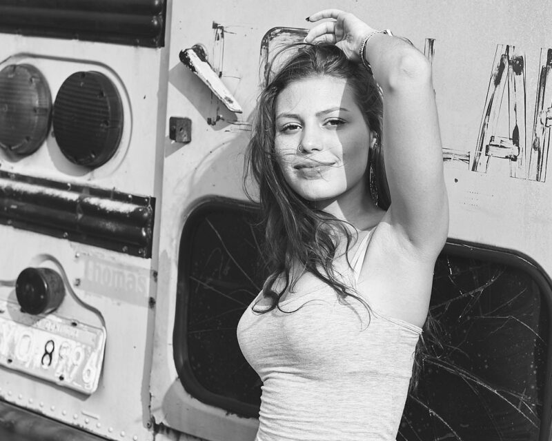 Retrato preto e branco de mulher ruiva passando a mão nos cabelos encostada em um ônibus antigo