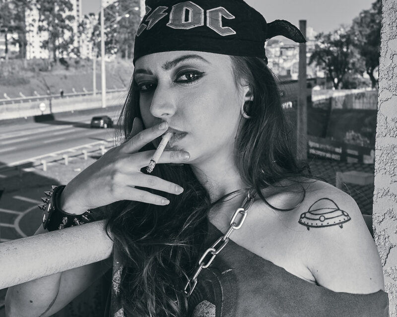 Mulher fumando na sacada de uma prédio, com uma rodovia ao fundo