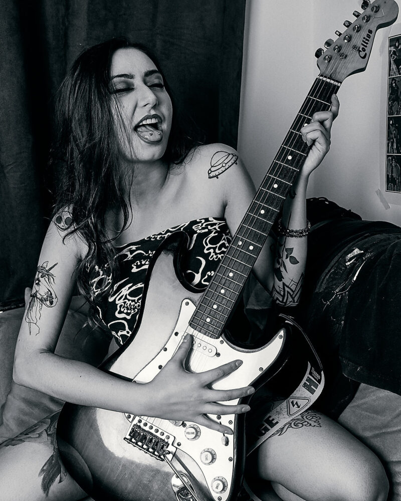 Mulher posando com uma guitarra em cima de um sofá
